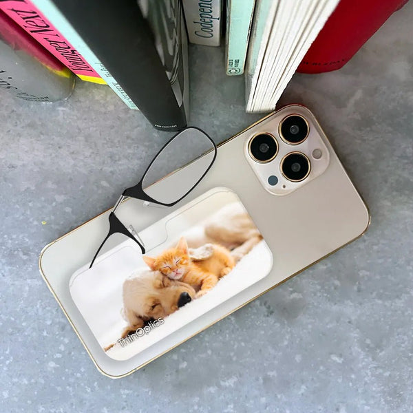 ThinOptics reading glasses rest on a smartphone with a golden retriever puppy and orange tabby kitten napping on the case.