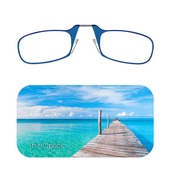 ThinOptics blue reading glasses folded atop a slim carrying case featuring a wooden pier extending over turquoise ocean water.