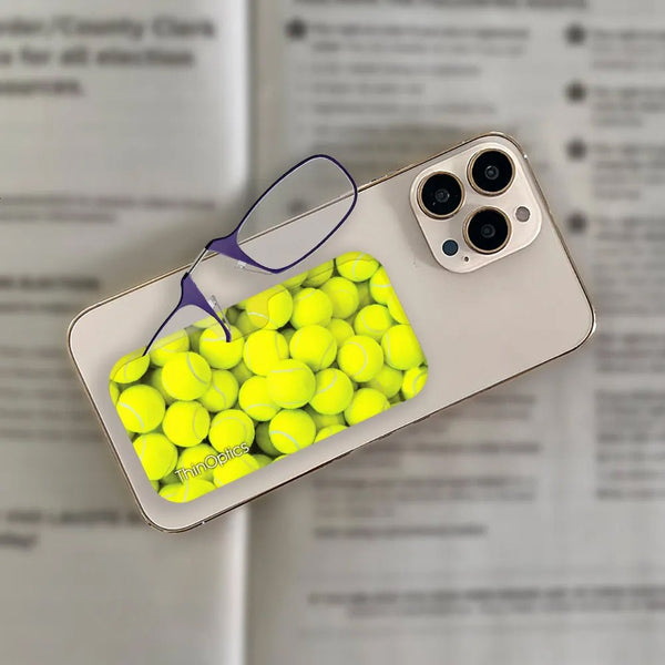 ThinOptics readers with vibrant tennis ball print rest on top of a smartphone and open book.