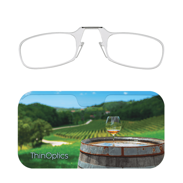 Silver ThinOptics reading glasses folded atop a case featuring a wine glass on a barrel in a vineyard.