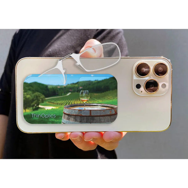Man holds ThinOptics reading glasses and case featuring a vineyard scene with a wine glass on a barrel.