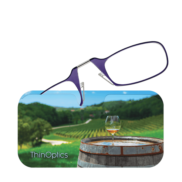 Purple ThinOptics reading glasses rest on a case depicting a vineyard scene with a glass of wine on a barrel.