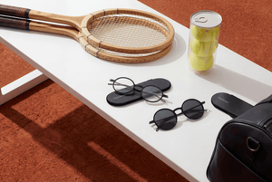 ThinOptics readers and reading sunglasses rest on a tennis bench with rackets and balls.