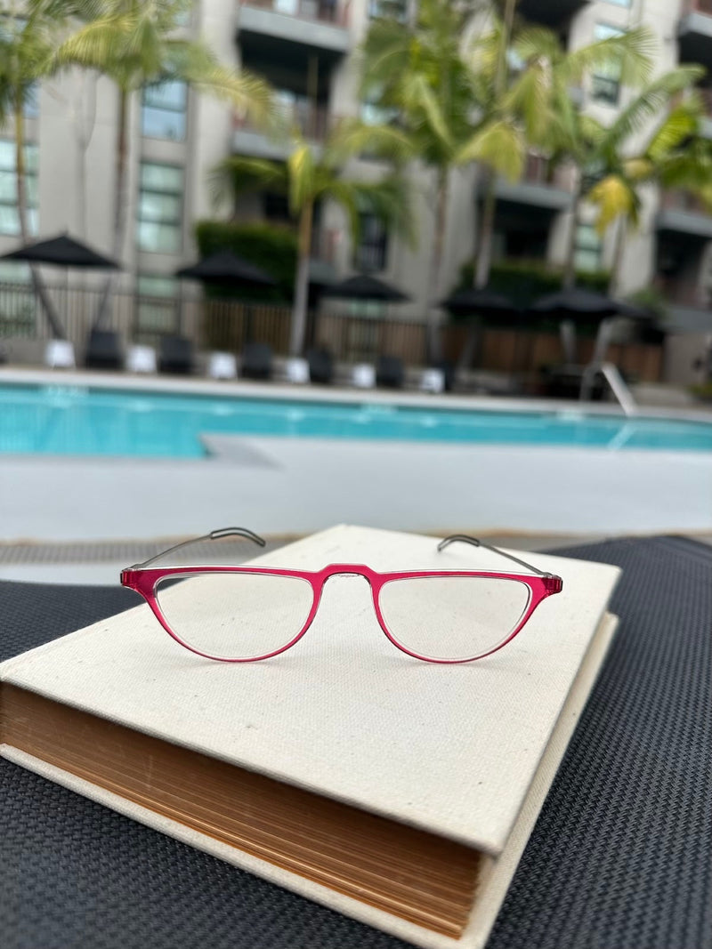 Red Crescent Reading Glasses resting on a book in front of a pool.