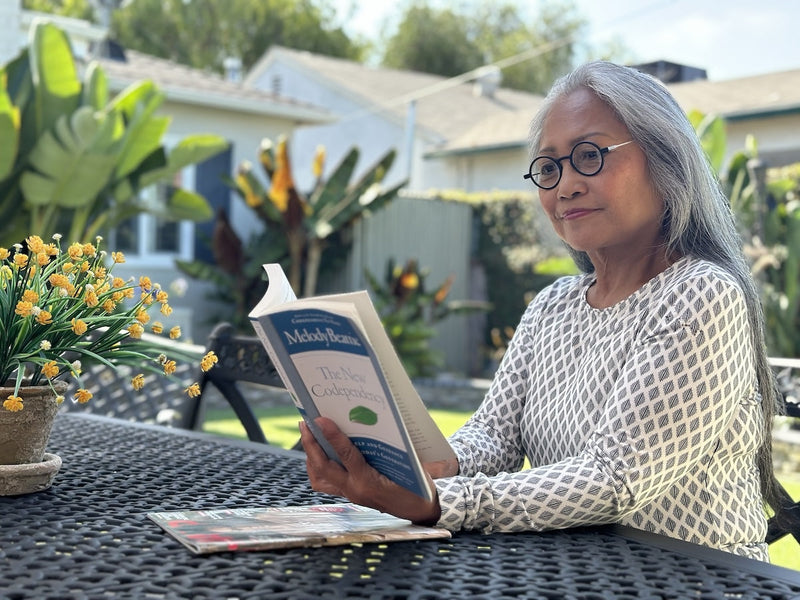 Woman sitting outdoors wearing round Manhattan Rx Prescription Glasses and reading a book.