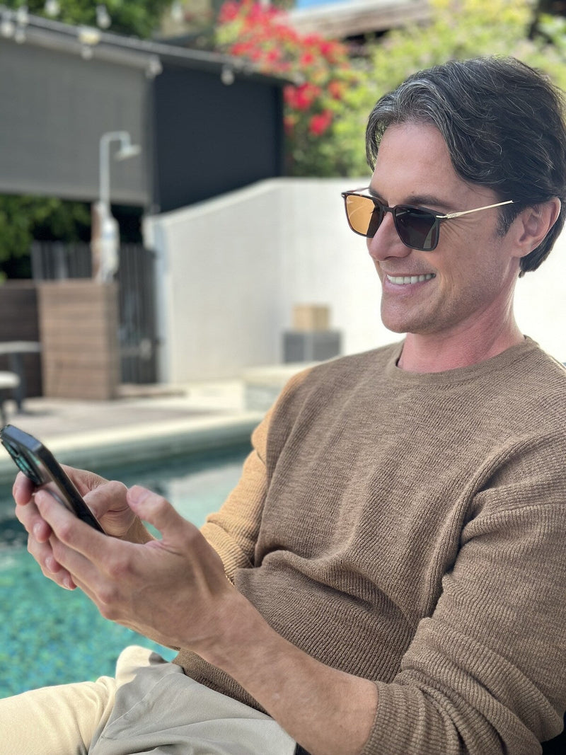 Man wearing ThinOptics Rx Prescription Glasses with Photochromic Lenses and reading outdoors on his phone.