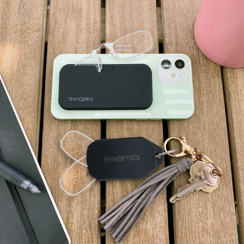 A phone with an attached Readers + Universal Pod Case next to a set of keys with an attaches Readers + Keychain Case.