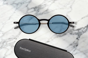 ThinOptics Manhattan Blue Light Blocking Reading Glasses + Milano Case against a marble counter.