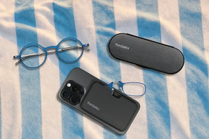 Blue ThinOptics glasses and cases rest beside a phone on a blue-and-white striped cloth.