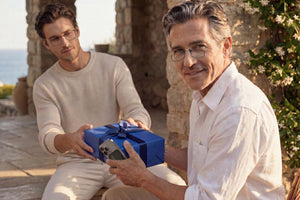 Man wearing ThinOptics reading glasses smiles while holding a smartphone and receiving a wrapped gift, highlighting readers as a thoughtful and practical present.