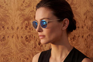 Woman wearing ThinOptics reading sunglasses outdoors against a wooden wall for glare-free close-up vision.