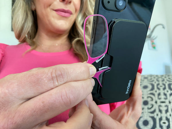 Woman removing Blushing Pink Readers from her iPhone with Black Universal Pod on back - Limited Edition ThinOptics Reading Glasses 