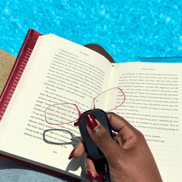 Woman relaxing by pool, book on lap, using Blushing Pink Spring Bloom Readers from black Keychain Case - Limited Edition ThinOptics Reading Glasses