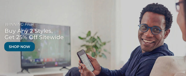 Man wearing blue reading glasses using smartphone while watching sports on TV