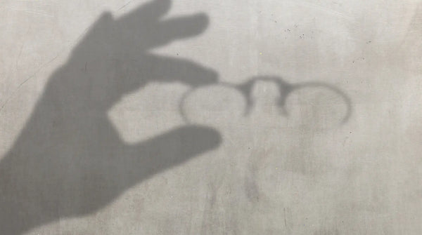 Shadow of a hand holding ThinOptics armless reading glasses cast on a concrete surface