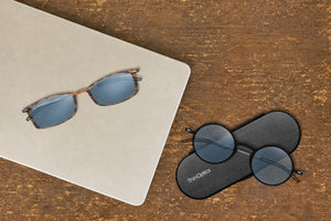 ThinOptics Brooklyn tortoise and Manhattan black blue light blocking glasses with Brooklyn case on a wood surface