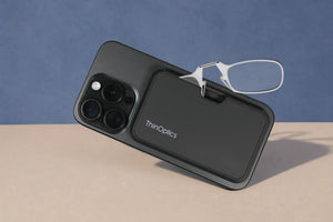 ThinOptics clear armless reading glasses peeking out of a black MagSafe phone case attached to the back of an iPhone