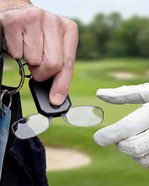 Hands opening a ThinOptics keychain case to reveal compact armless reading glasses, with a golf glove and green fairway in the background