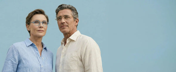 Woman wearing ThinOptics blue round prescription glasses and man wearing clear rectangular frames against a light blue background