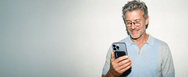Smiling man wearing ThinOptics black armless readers looking at his phone with a ThinOptics Pod case attached