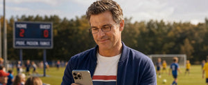 Man wearing ThinOptics brown rectangle reading glasses checking his phone on the sideline of a youth soccer game