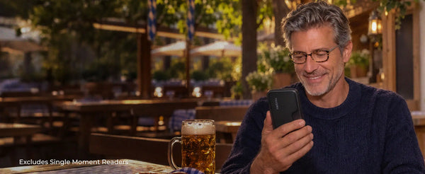 Man wearing ThinOptics reading glasses checking his phone with a ThinOptics Pod case at an outdoor beer garden with a stein of beer