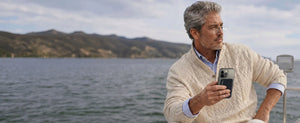 Man wearing ThinOptics reading glasses holding a phone with a ThinOptics case on a boat near coastal hills