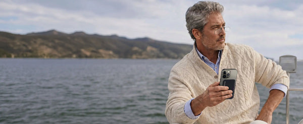 Man wearing ThinOptics reading glasses holding a phone with a ThinOptics case on a boat near coastal hills