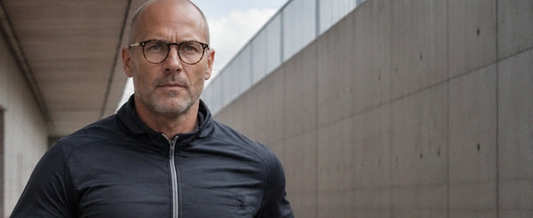 Man wearing ThinOptics tortoise round prescription glasses in an athletic jacket against a concrete wall outdoors