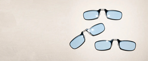 Three ThinOptics Moment blue light blocking armless readers shown from different angles on a cream background