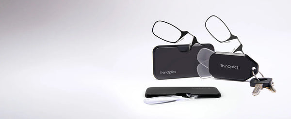 ThinOptics Moment Readers with black Pod case, black keychain case with keys, and clear readers in a slim case on white background