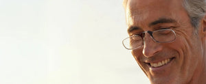 Close-up of a smiling man wearing ThinOptics Moment black armless reading glasses in warm natural light