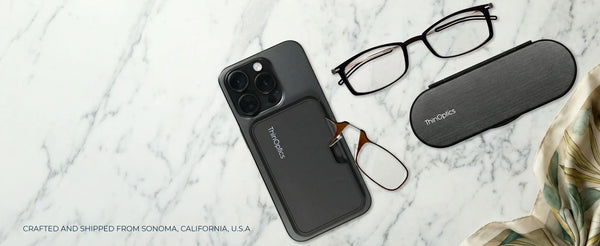 ThinOptics phone case with tortoiseshell armless readers, black rectangular reading glasses, and a slim oval case arranged on a white marble surface