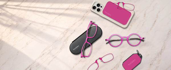 ThinOptics pink reading glasses collection flatlay on marble surface featuring rectangle and round frames with Brooklyn case, phone case, and keychain case