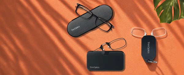 ThinOptics flatlay of rectangle glasses with case, black Pod case with armless readers, and navy keychain case on an orange surface