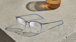 ThinOptics purple round prescription glasses with thin metal temples resting on a concrete surface in warm sunlight