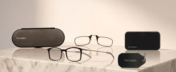 ThinOptics reading glasses and protective cases displayed on marble surface including folding readers, full-frame glasses, and compact keychain case