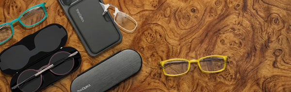 ThinOptics reading glasses collection with cases and phone attachment on wood table