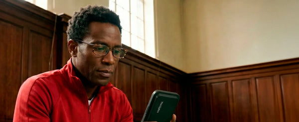 Man wearing ThinOptics reading glasses looking at smartphone with slim phone-mounted case in indoor setting