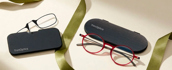 ThinOptics reading glasses with slim cases and ribbon on neutral background