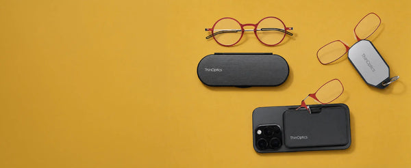 ThinOptics red Manhattan glasses, Brooklyn case, keychain case, and MagSafe phone case with red armless readers on a yellow background