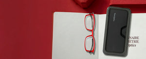 Red ThinOptics reading glasses and slim black carrying case displayed on open book with red background accents