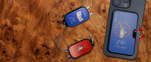 ThinOptics USA 250th anniversary limited edition collection — red, white, and blue keychain cases and phone case with armless readers, displayed on a burl wood surface