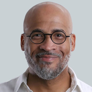 "Portrait of a smiling bald man with a salt-and-pepper beard wearing round glasses." 
